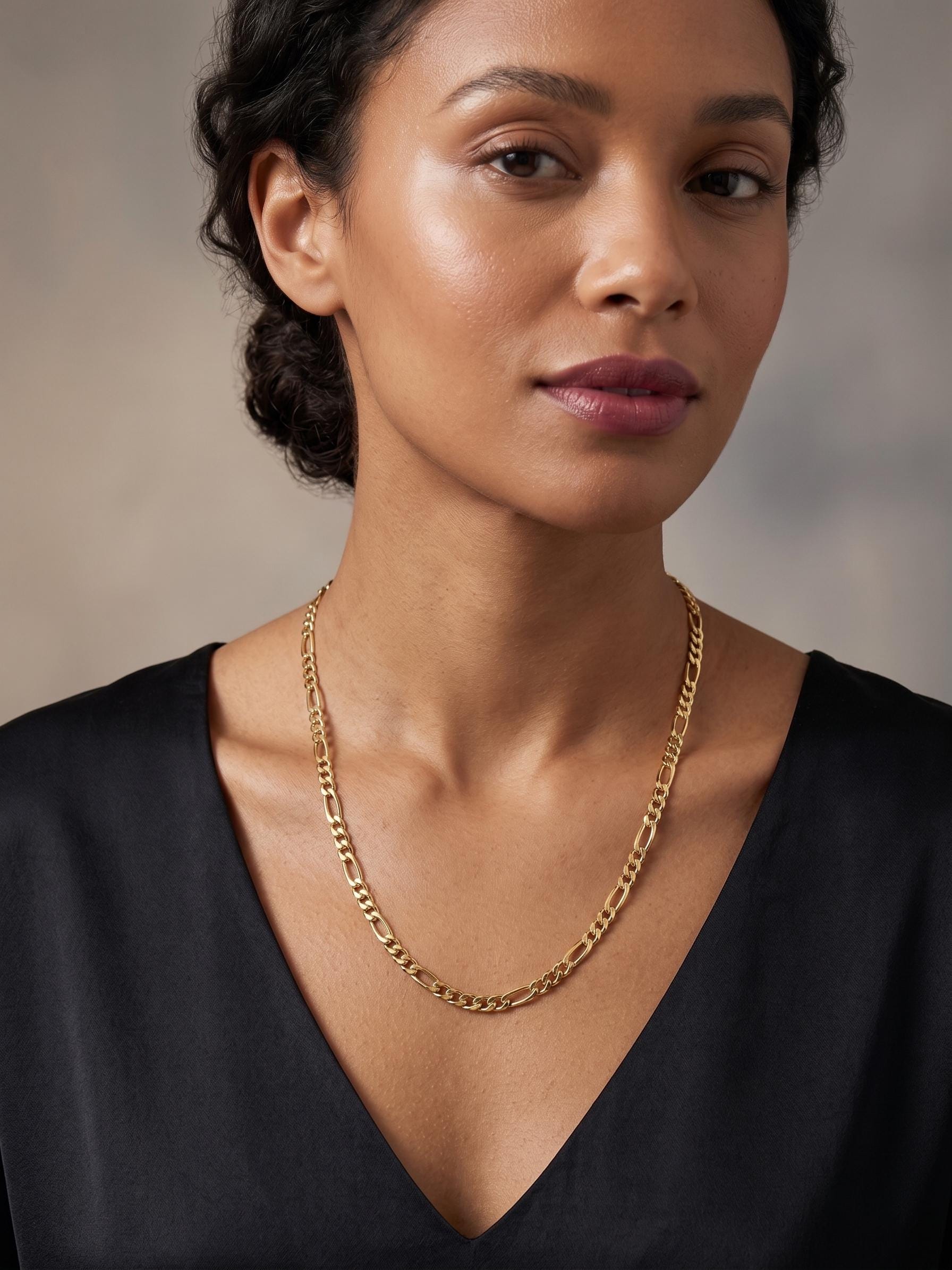 Close-up of a 14K solid gold Figaro chain necklace worn on a female model, featuring alternating flat links with a high-polish shine.
