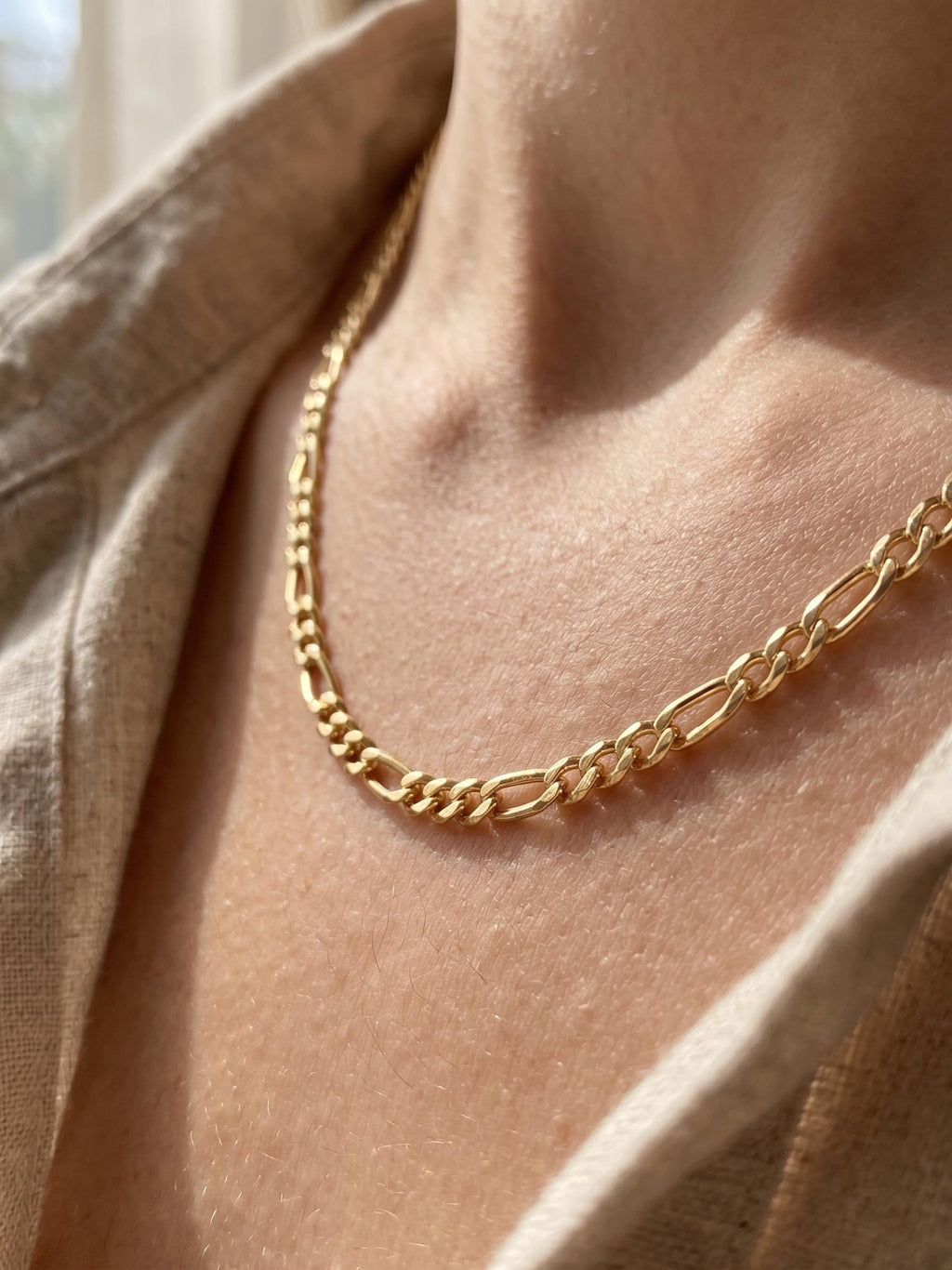 Close-up of a 14K gold Figaro chain necklace worn on a woman’s neck, featuring polished alternating links in a classic elegant design.